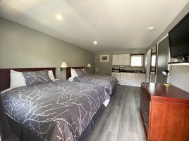 Un dormitorio con dos camas, un aparador de madera, una kitchenette y un televisor.
