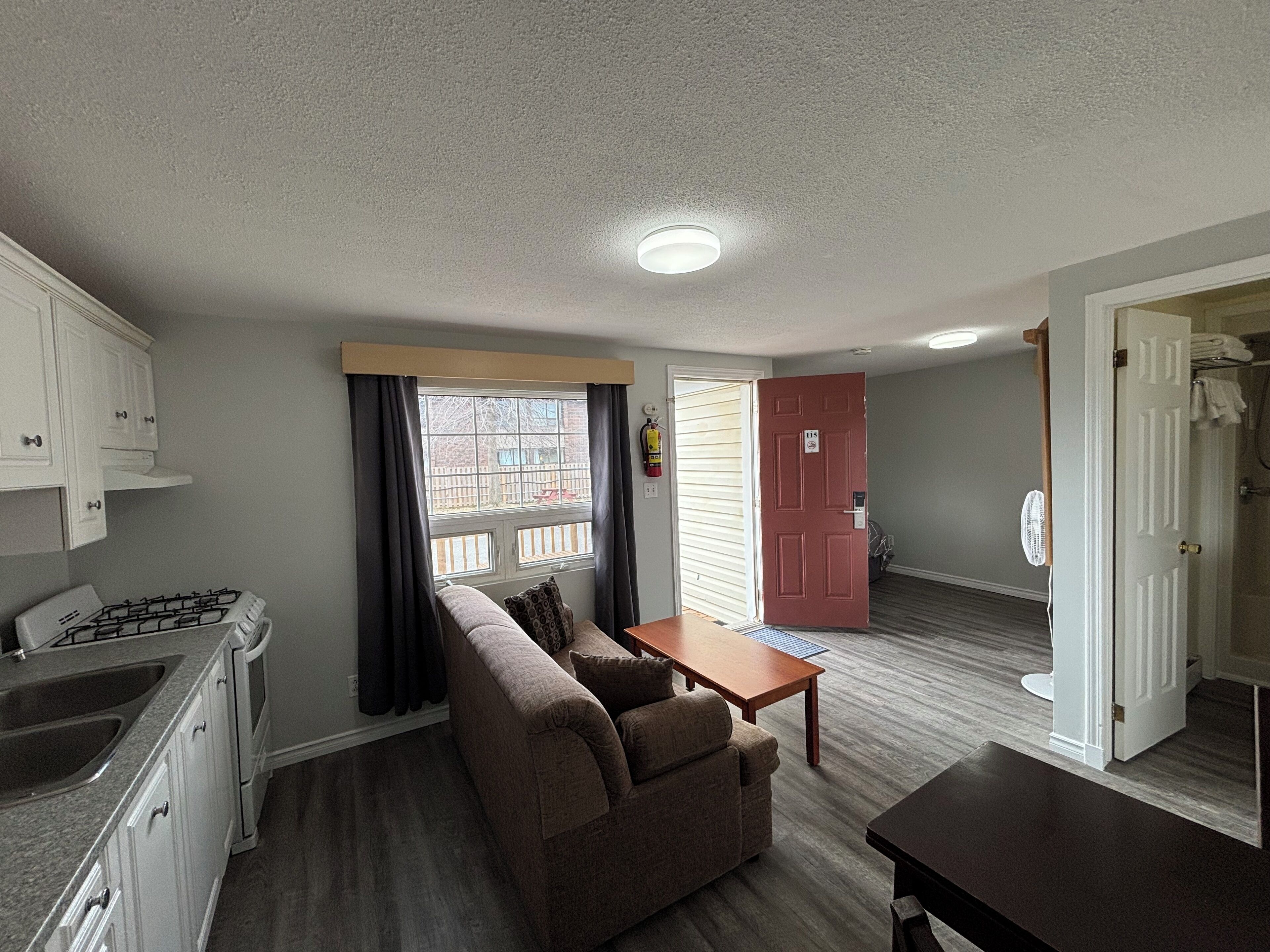 Un espacio habitable compacto con kitchenette, un sofá, una mesita y una puerta que da al baño.