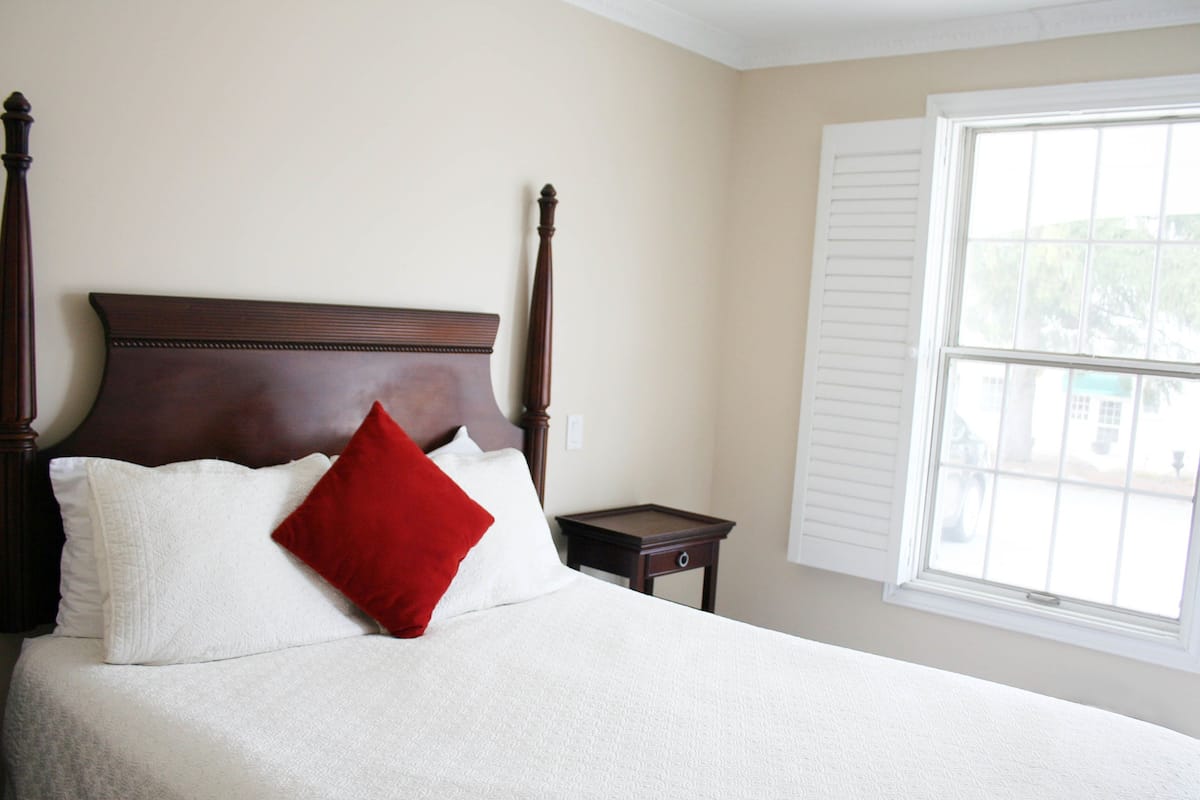A neatly made bed with a wooden headboard, a small bedside table, and a window with white shutters.