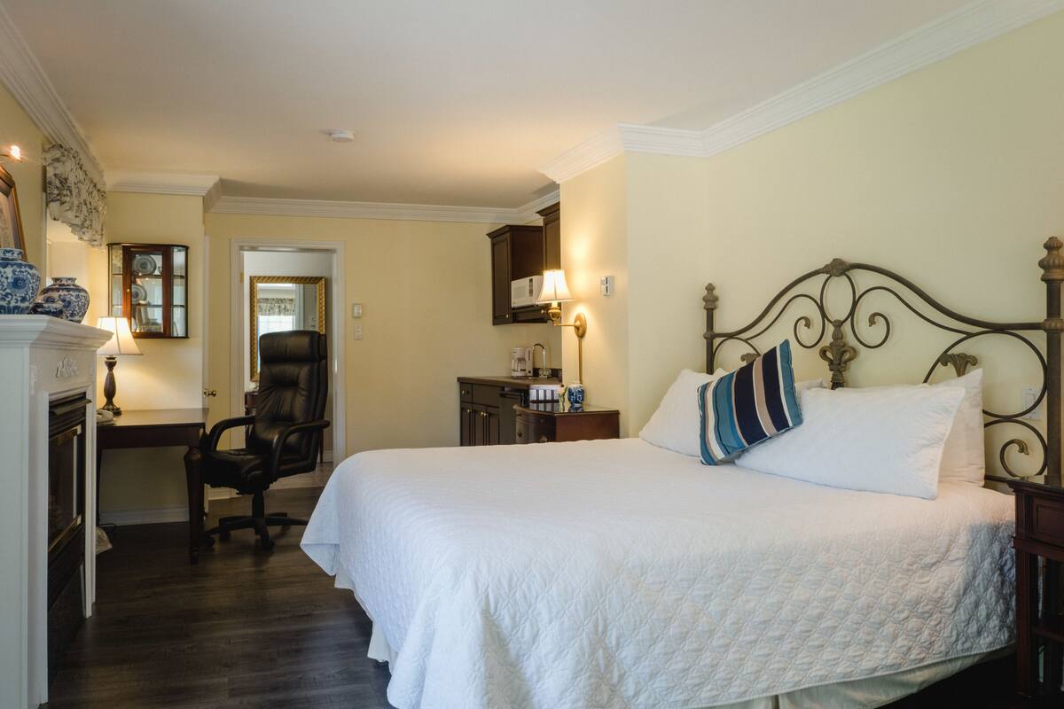 A neatly arranged bedroom with a large bed, a chair, a desk, and a mirror.