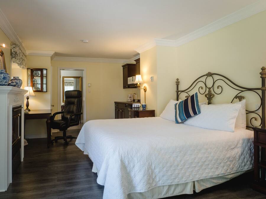 A neatly arranged bedroom with a large bed, a chair, a desk, and a mirror.