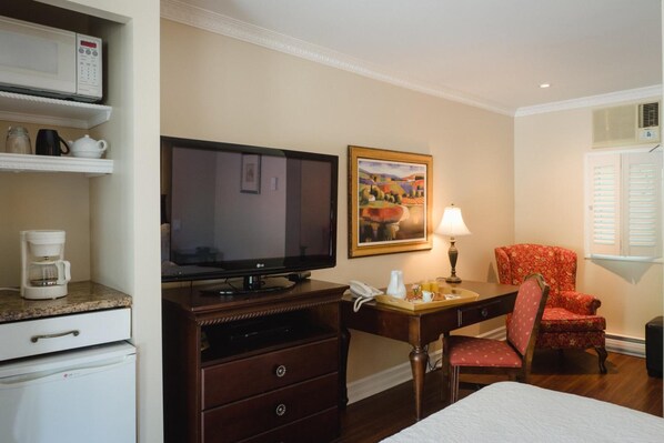Habitación de hotel con cama, escritorio con lámpara, televisor, cafetera y una silla.
