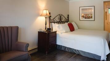 A hotel room with a bed, a bedside table with a lamp, a chair, and a framed picture on the wall.
