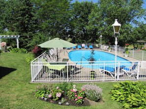 A swimming pool with a white fence, lounge chairs, and a lamp post.