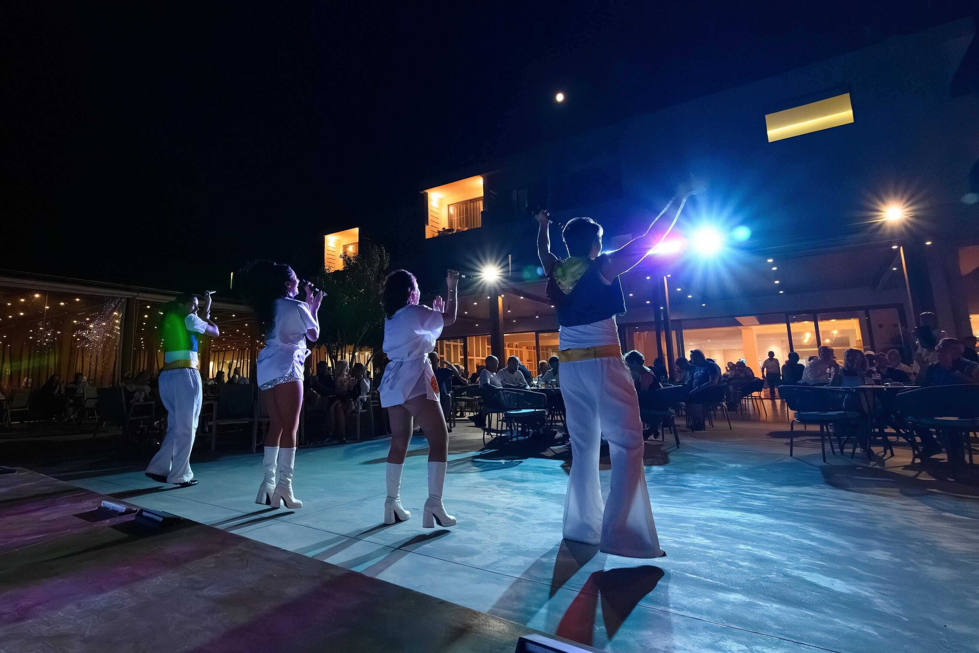 A stage with performers, an audience, and outdoor seating.