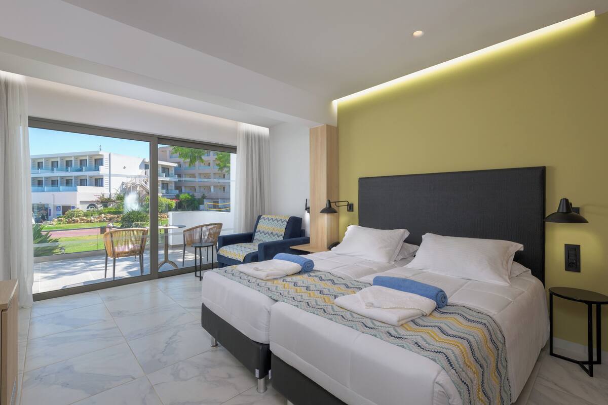 Une chambre d’hôtel moderne dotée d’un grand lit, d’un balcon avec un coin repas et offrant une vue sur le paysage urbain.