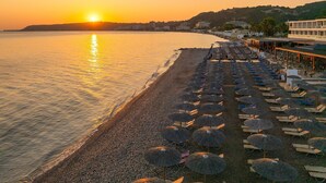 Una platja amb files de papereres i gandules, un capvespre, i edificis al fons.
