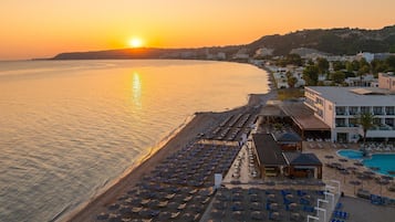 A beachside hotel with a sunlit ocean view, a pool, and a row of sun loungers.
