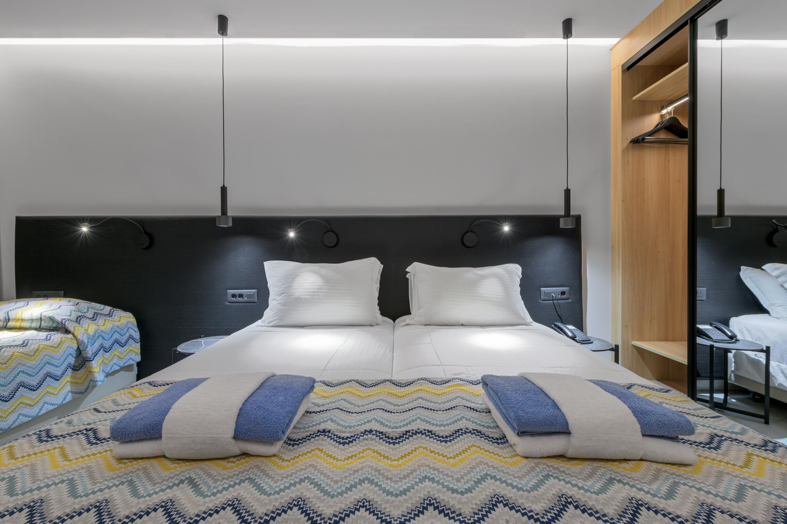 Una habitación de hotel moderna con una cama grande, mesitas de noche, un armario y un espejo.