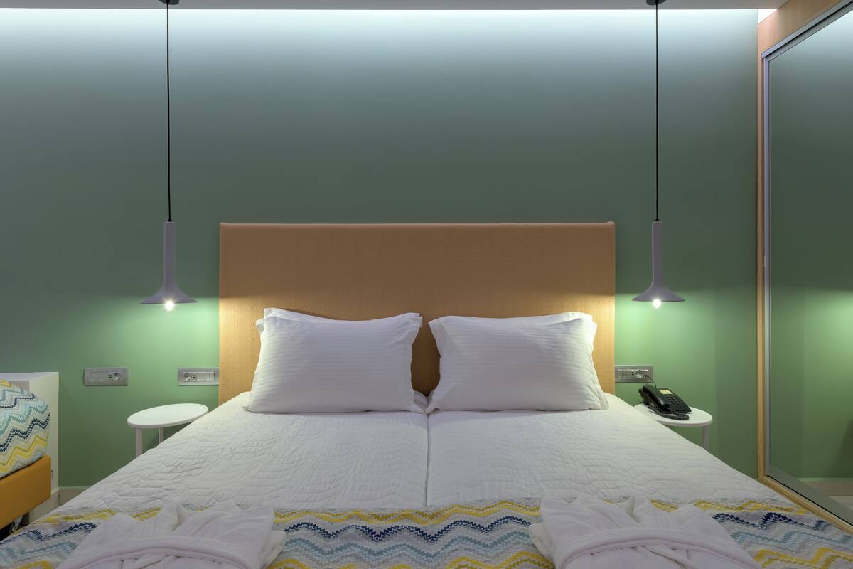 Un lit bien fait, avec du linge de lit blanc, une tête de lit en bois et une table de chevet sur laquelle se trouve un téléphone.