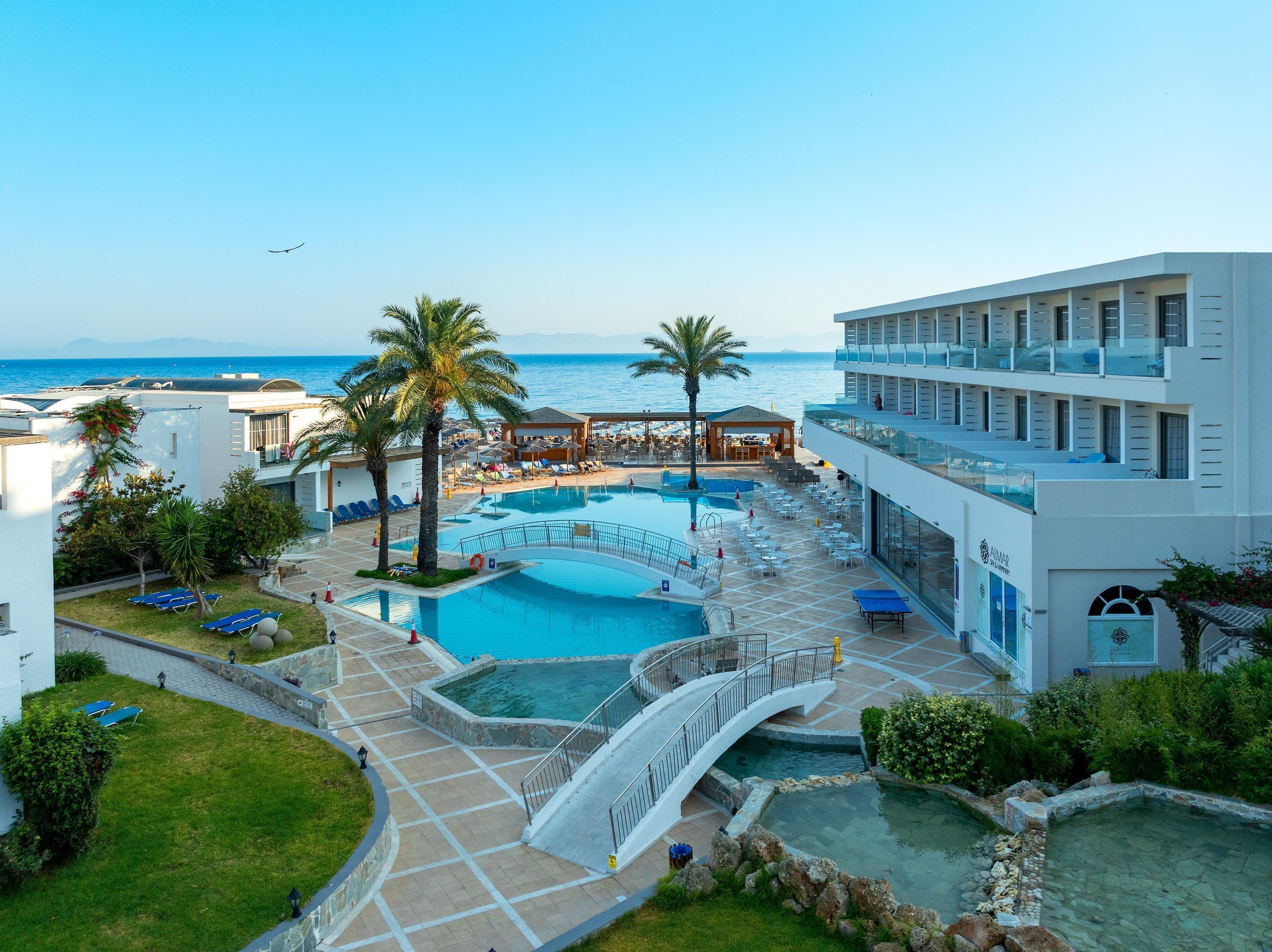 Un resort con una amplia zona de piscina, palmeras y vistas al mar.