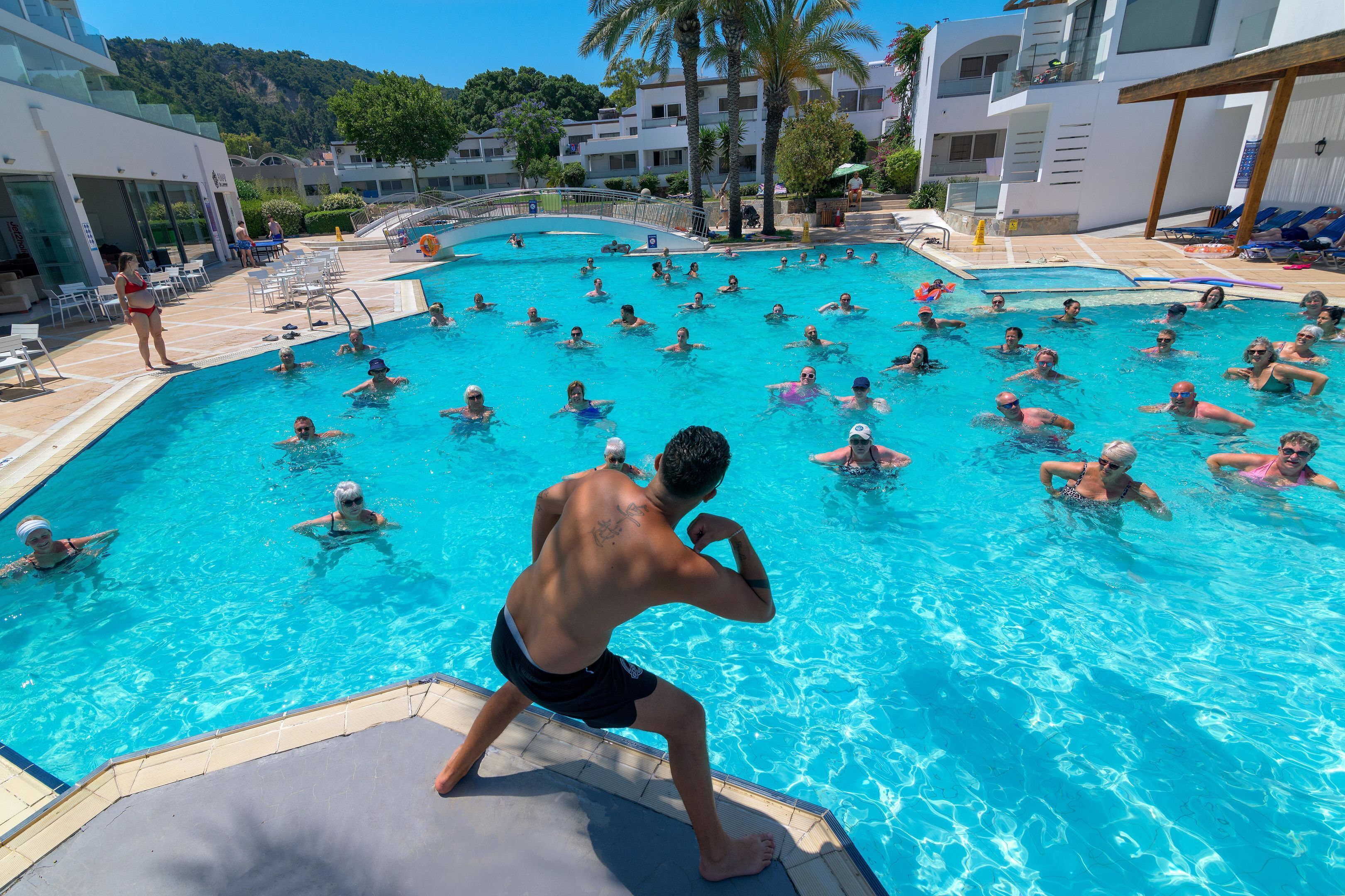 A swimming pool with multiple people in the water, surrounded by lounge chairs and umbrellas.
