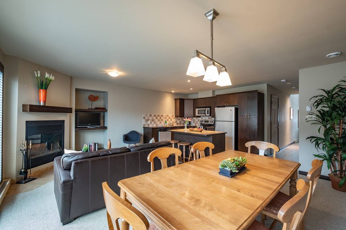 A modern kitchen with dark wood cabinets, a central island, and a dining area with a wooden table and chairs.