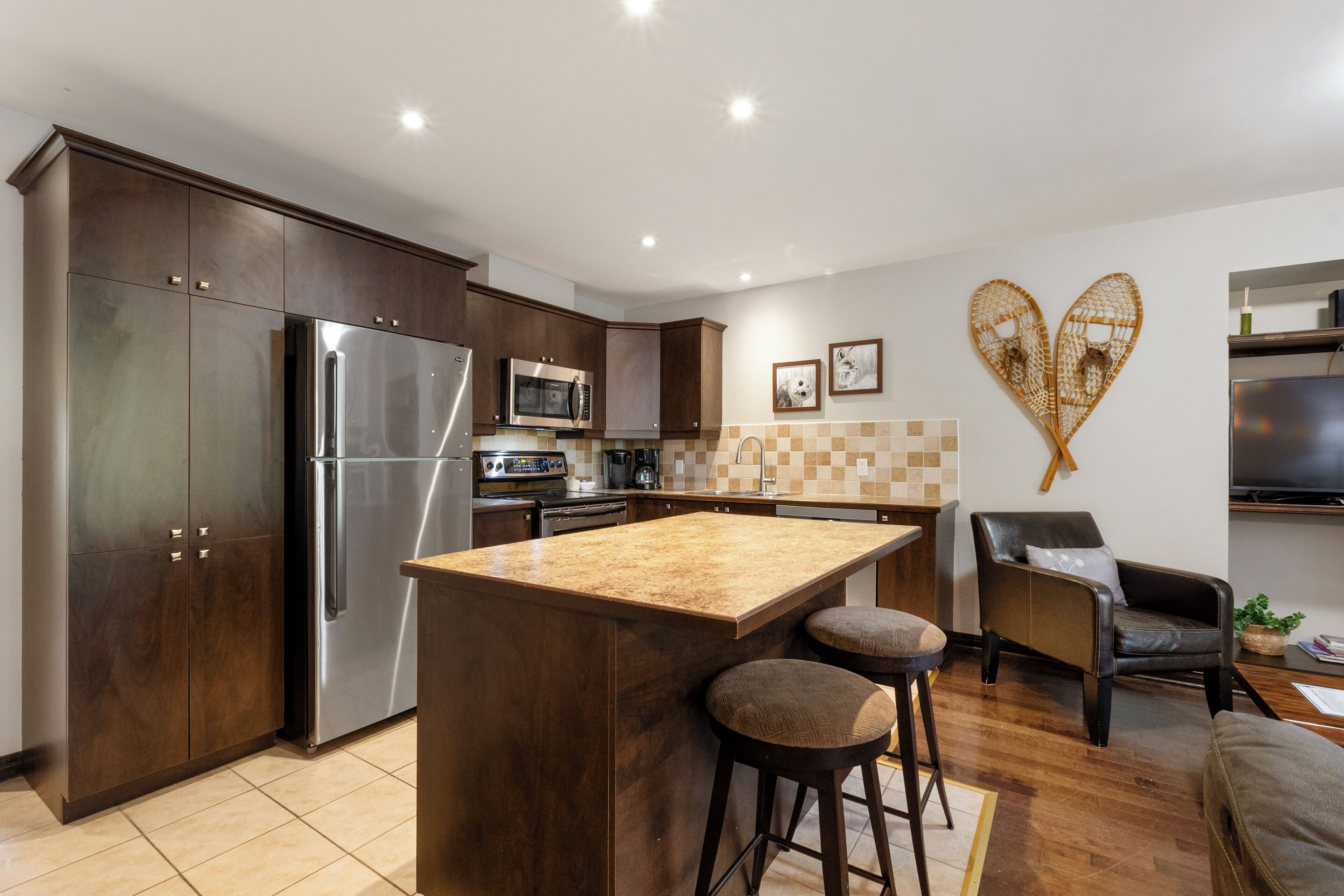 Una cucina moderna con mobili in legno scuro, elettrodomestici in acciaio inox, un'isola centrale con sgabelli e una decorazione a forma di cuore sulla parete.