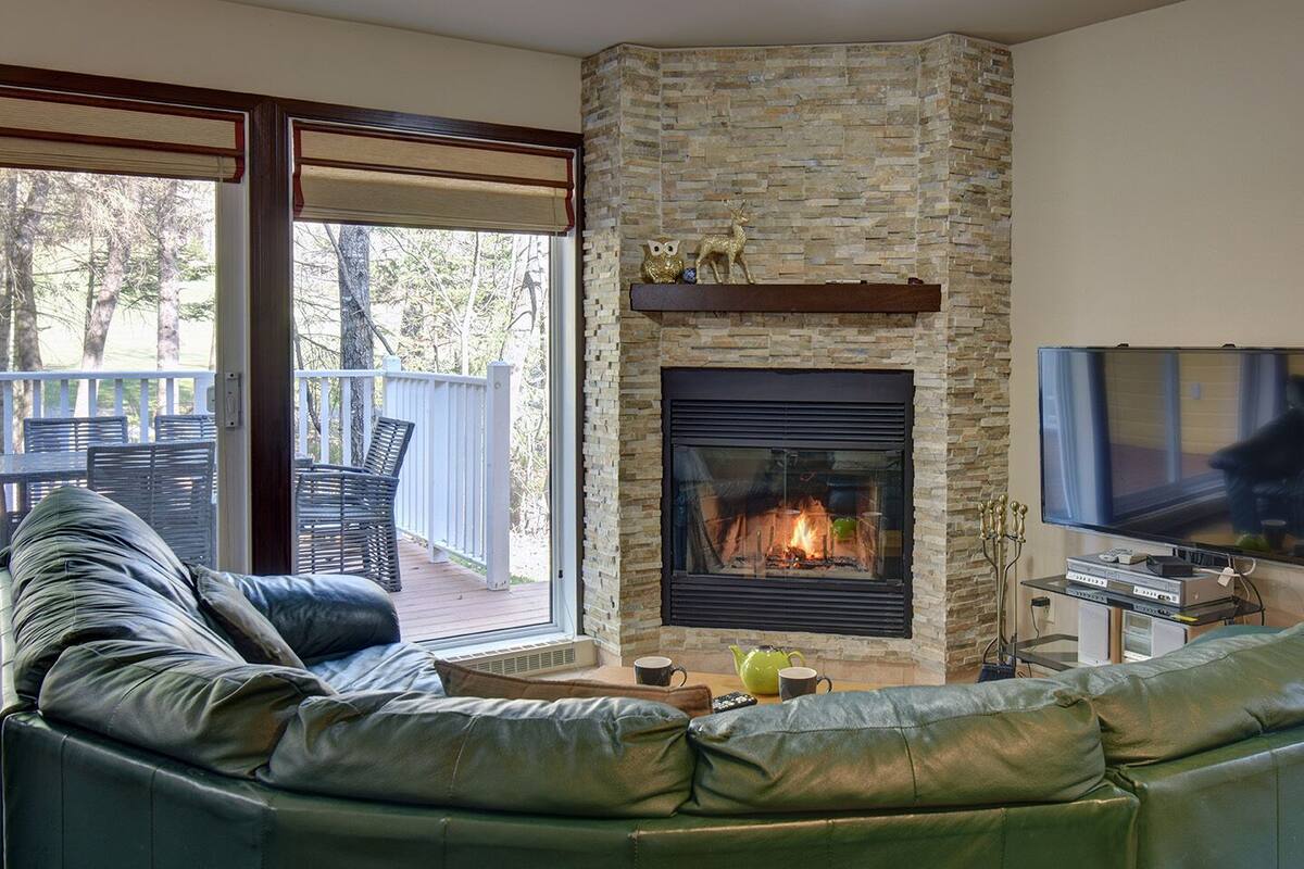 A living room with a stone fireplace, a green leather sofa, and a television mounted on the wall.