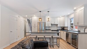 Una cocina moderna con gabinetes blancos, electrodomésticos de acero inoxidable y una isla central con taburetes de bar.