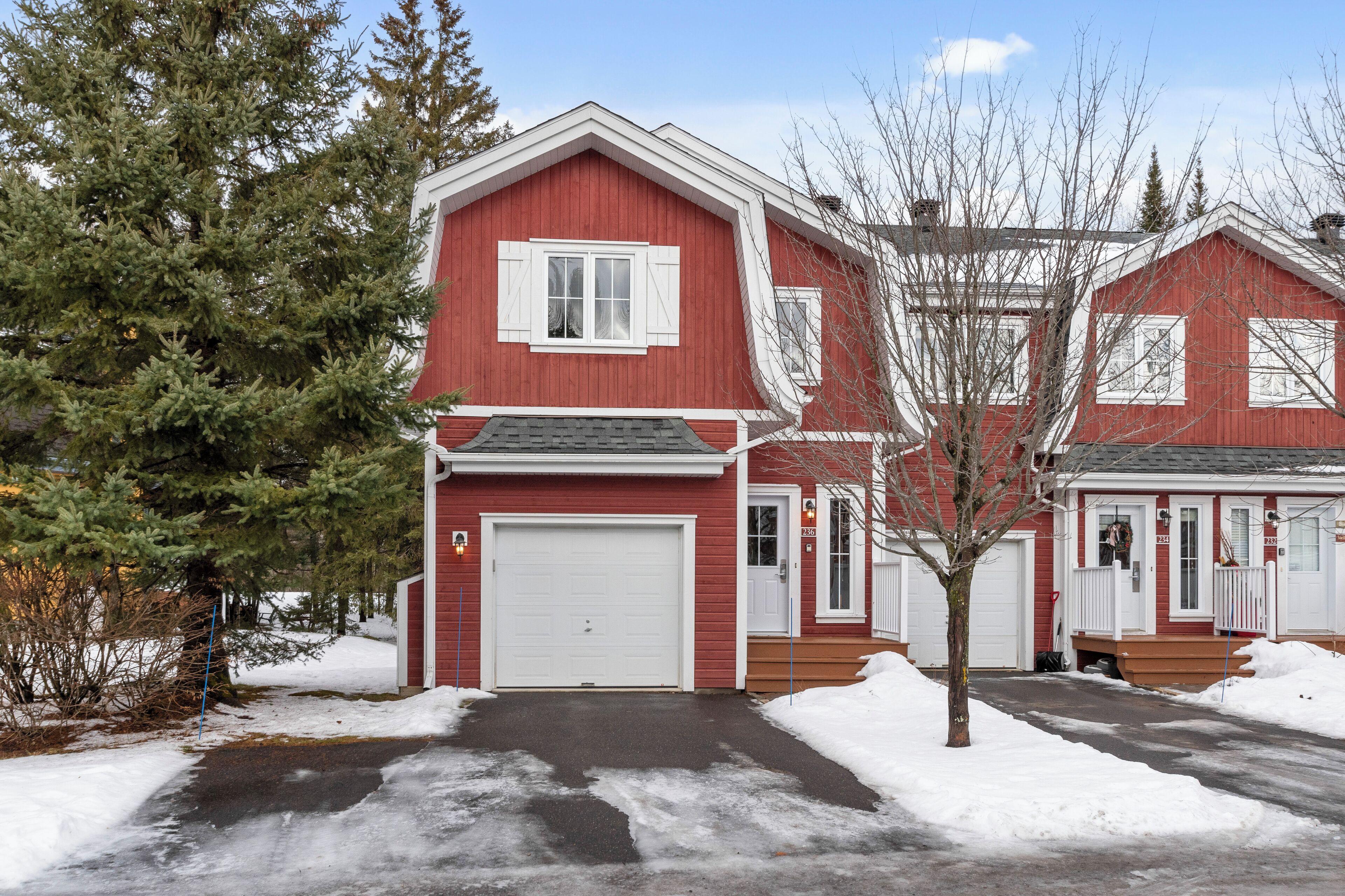 A red two-story house with a white garage door, a front porch, and a snow-covered driveway.