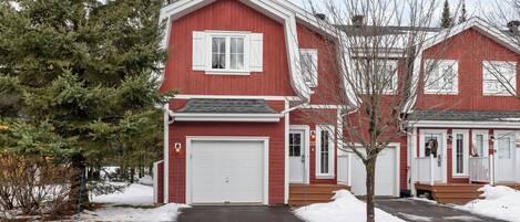 A red two-story house with a white garage door, a front porch, and a snow-covered driveway.