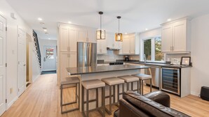 Una cocina moderna con una isla central, taburetes de bar, electrodomésticos de acero inoxidable e iluminación colgante.
