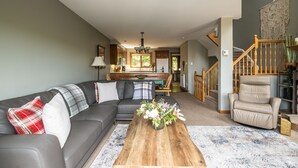Ein modernes Wohnzimmer mit einem grauen Modulsofa, einem Couchtisch mit floraler Dekoration und einer Treppe, die in eine obere Etage führt.