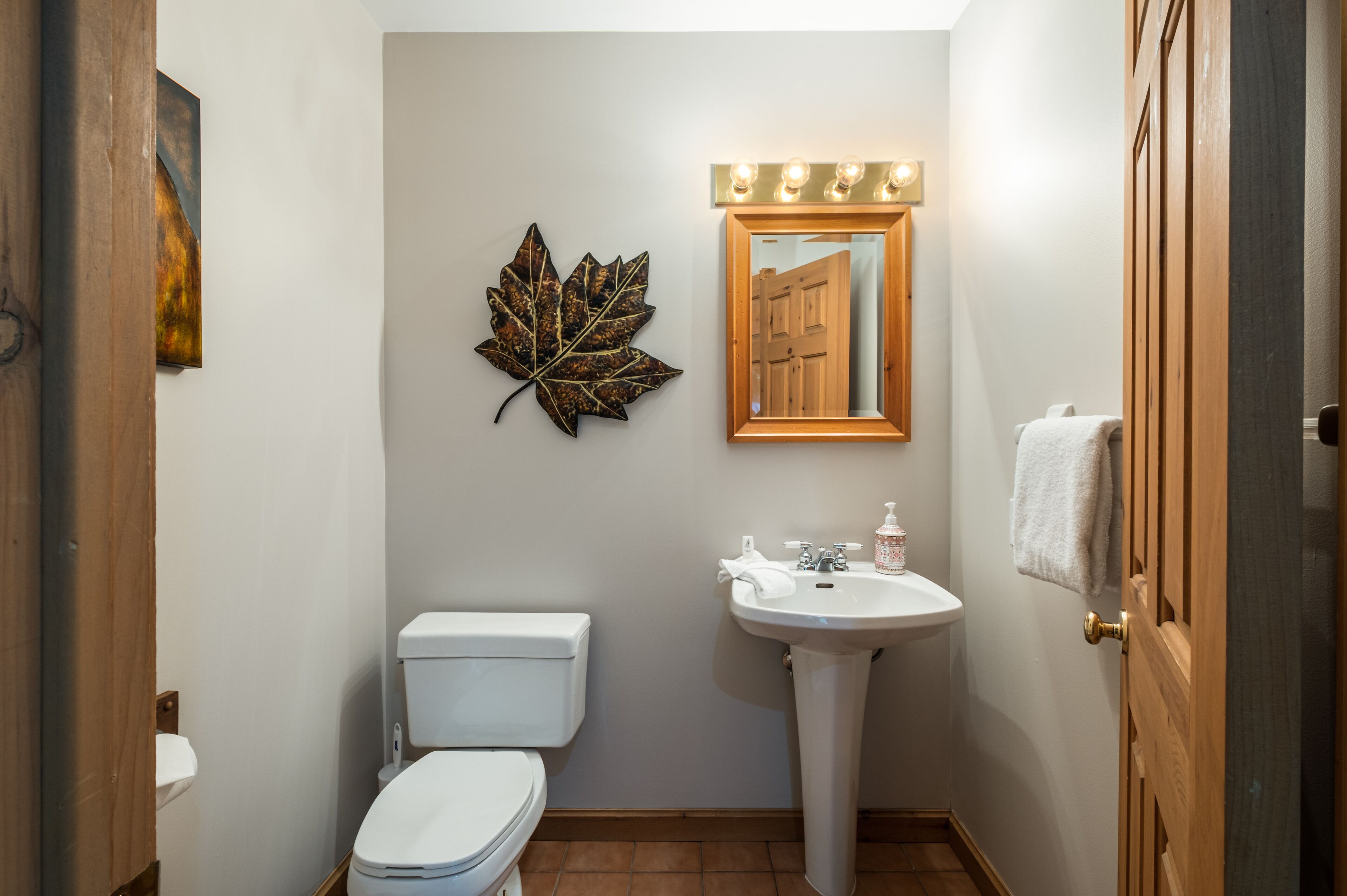 A compact bathroom with a toilet, sink, and a decorative leaf on the wall.