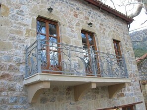 A stone building with a balcony featuring wrought iron railings and wooden-framed windows.