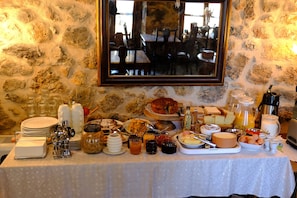 A breakfast buffet with various food items and utensils on a table against a stone wall.
