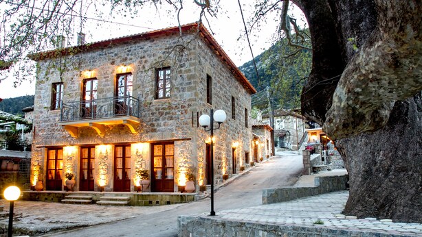 A stone building with a balcony, illuminated windows, and a paved pathway. - Arxontiko Kefalari (Sikyona)