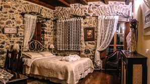 A rustic bedroom with a stone wall, a wooden bed, and a window with curtains. - Arxontiko Kefalari (Sikyona)