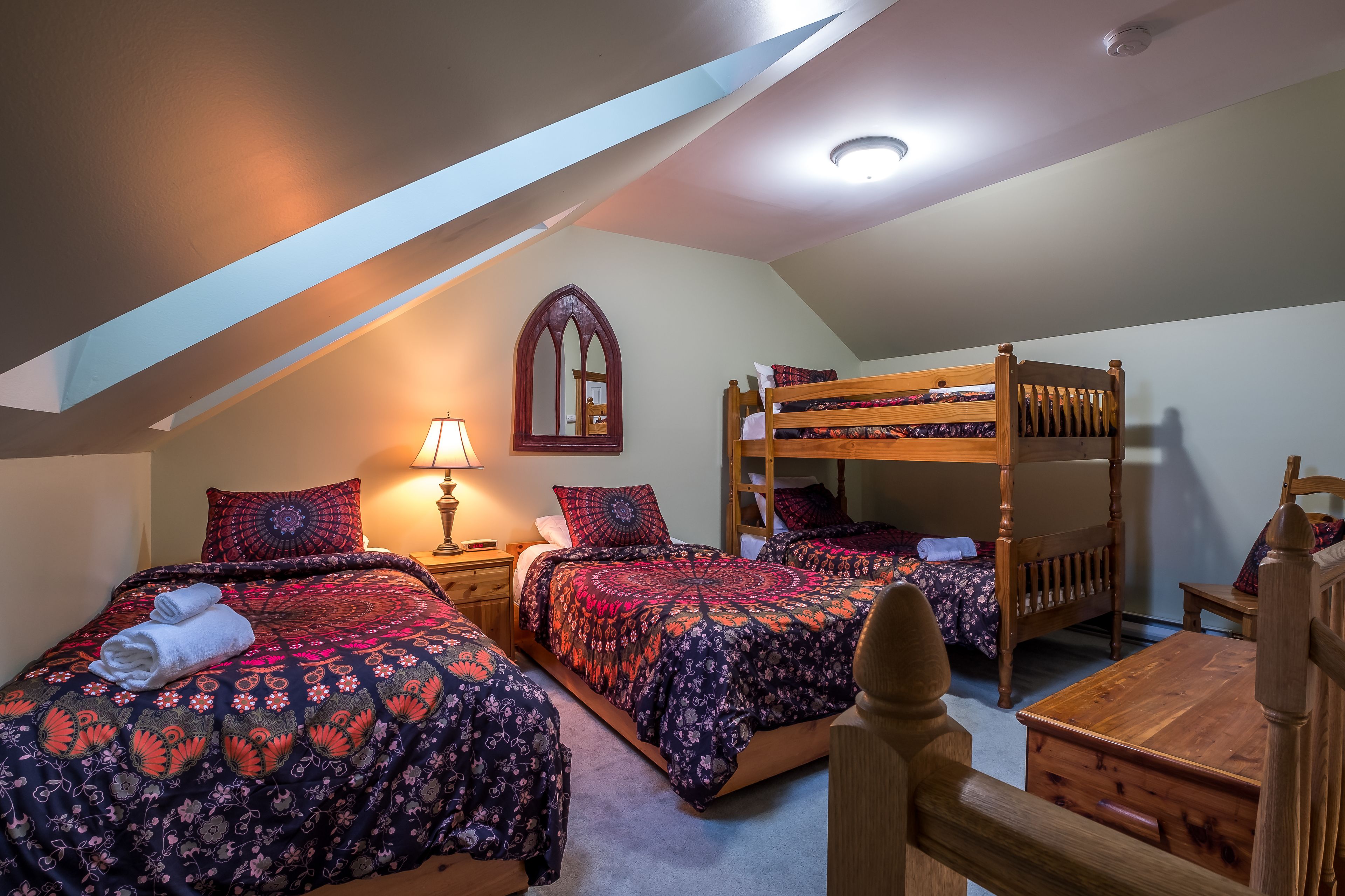 Ein gemütliches Schlafzimmer unter dem Dach mit zwei Betten, einem Schlafstapelbett, einem Schreibtisch und einer Lampe.