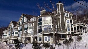 Una casa grande de varios pisos con una chimenea destacada, múltiples ventanas y un balcón.