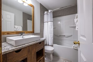 A modern bathroom with a white sink, wooden vanity, a large mirror, a white toilet, and a shower with a white curtain. - Le Boisé - RVMT (Mont-Tremblant)
