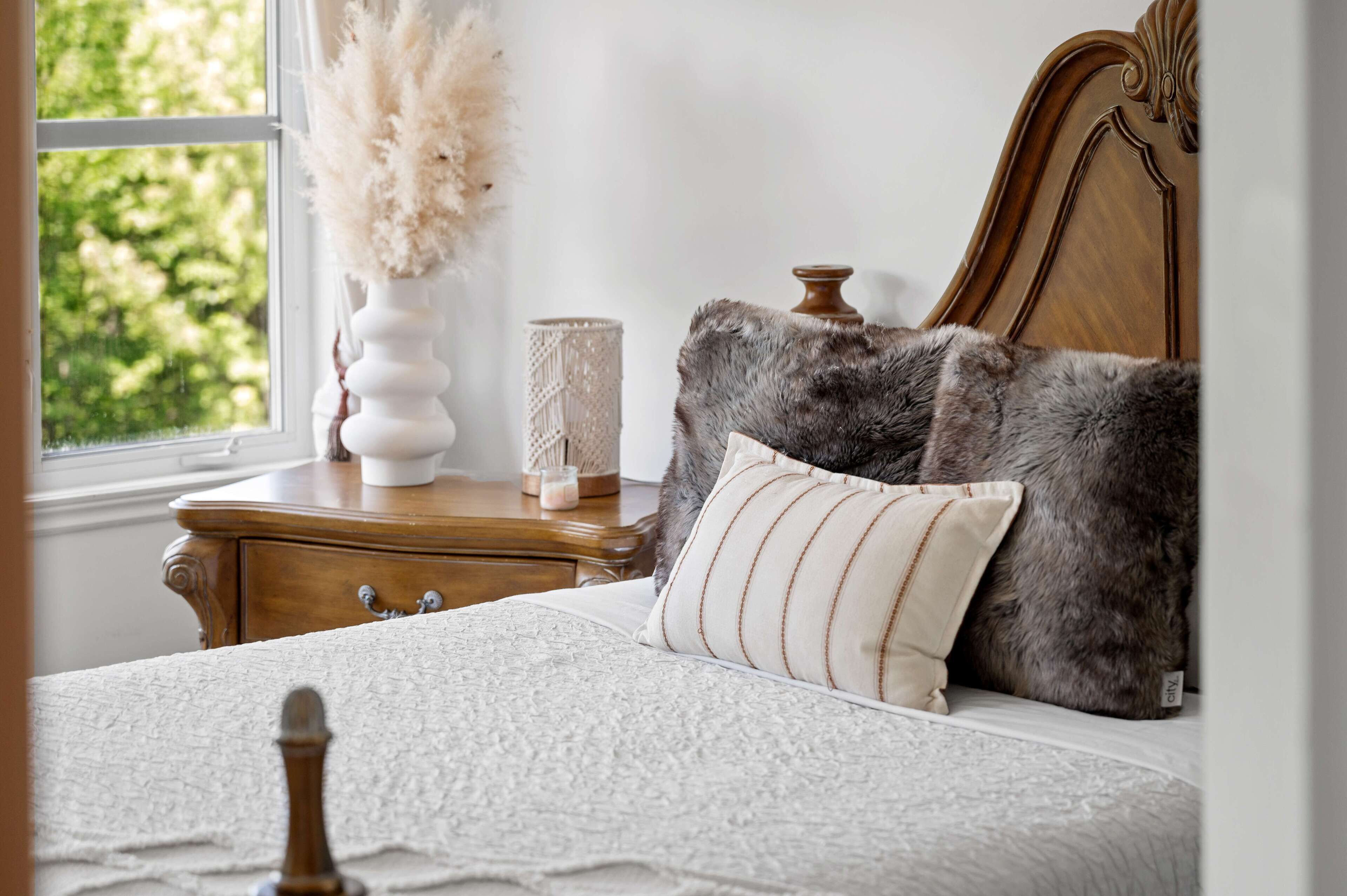 Une chambre à coucher avec une tête de lit en bois, un couvre-lit blanc et une fenêtre donnant sur un paysage verdoyant.