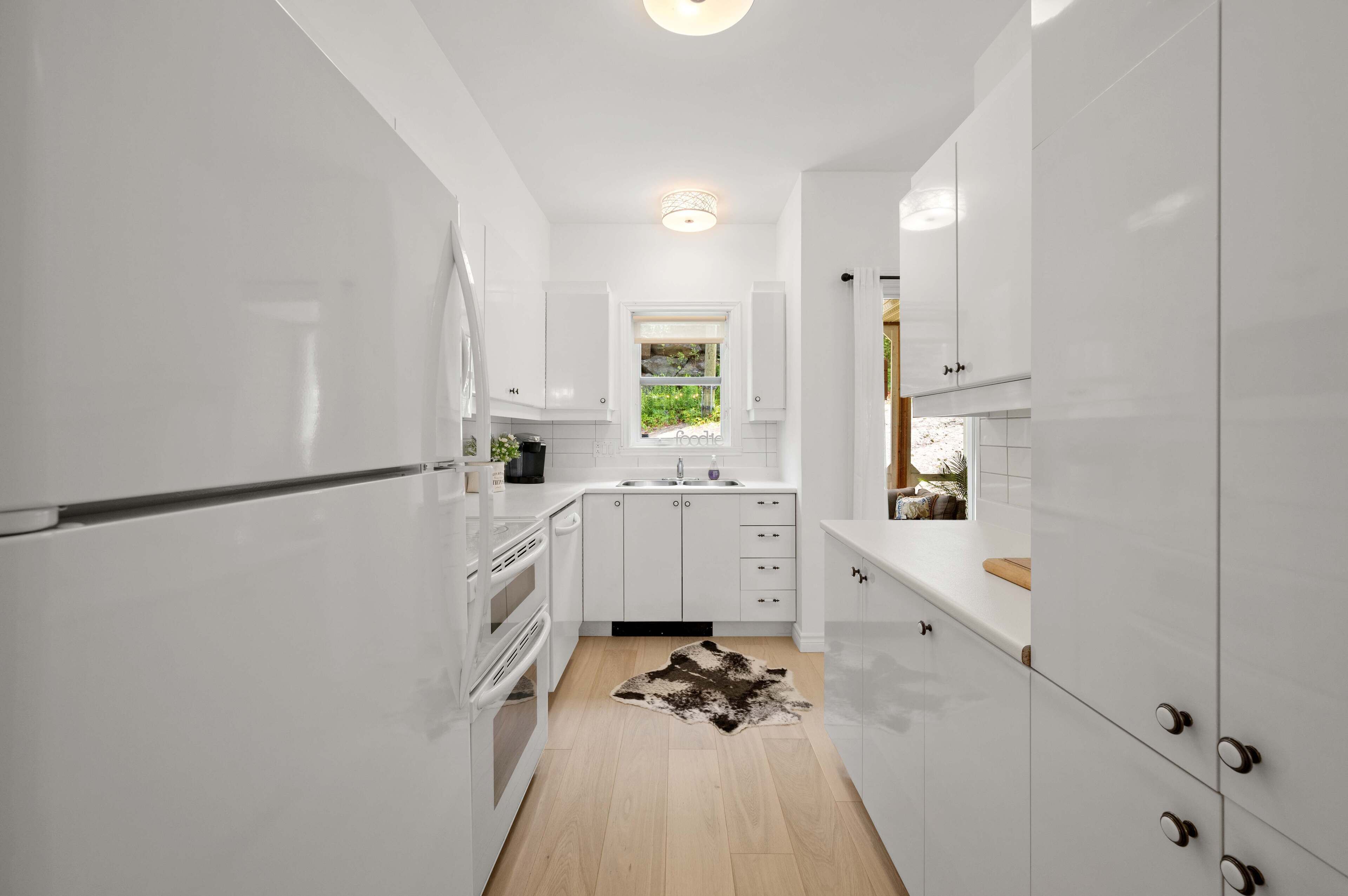 A modern kitchen with white cabinetry, a built-in oven, and a window providing a view of greenery outside.