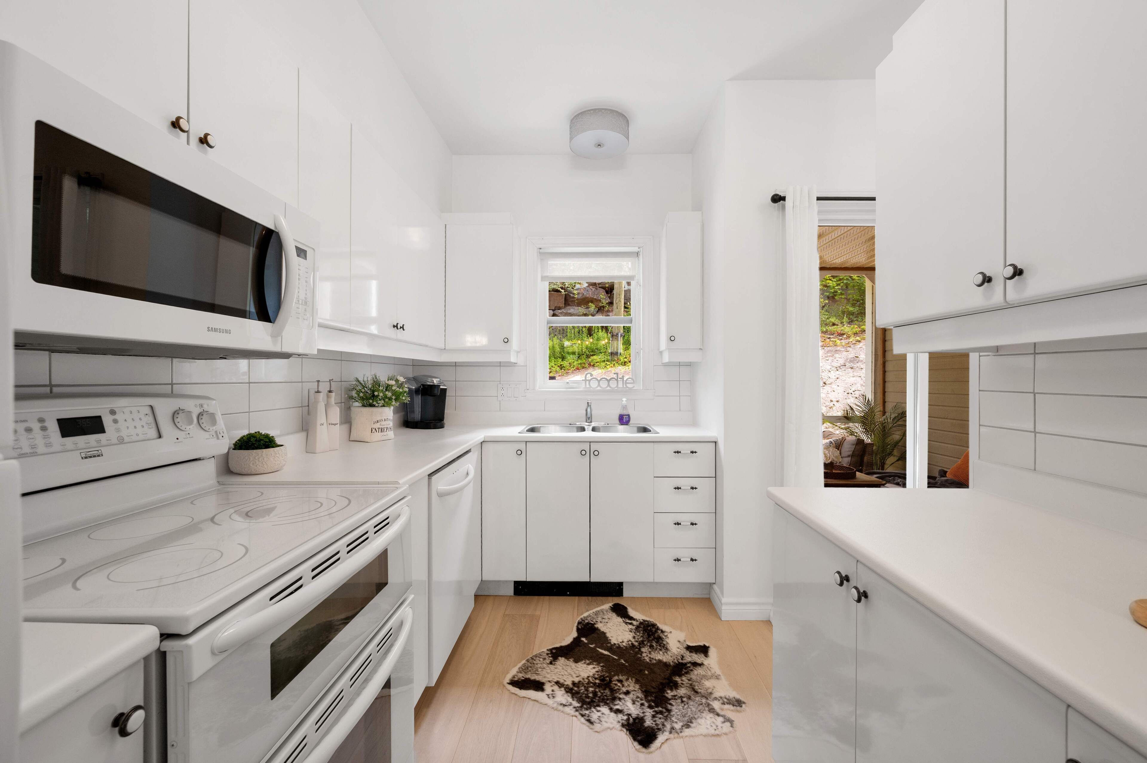 A compact kitchen with white cabinetry, a built-in microwave, a stove, and a sink.