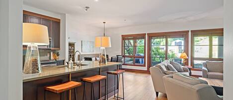 A modern kitchen with a central island, bar stools, and a dining area with a sofa and table.