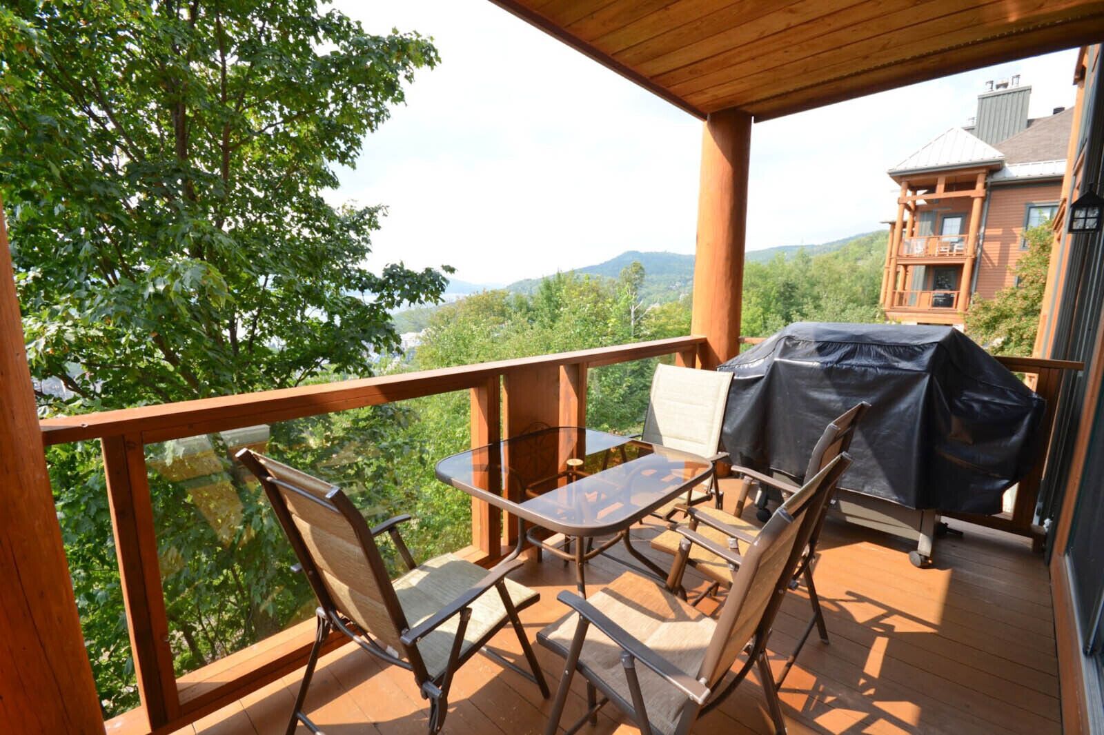 Une terrasse en bois avec une table et des chaises, un barbecue et une vue sur un paysage montagneux.