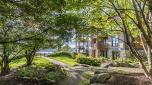 A modern house with a stone facade, large windows, and a well-maintained garden with a pathway leading to the entrance. - L'Equinoxe – RVMT (Mont-Tremblant)