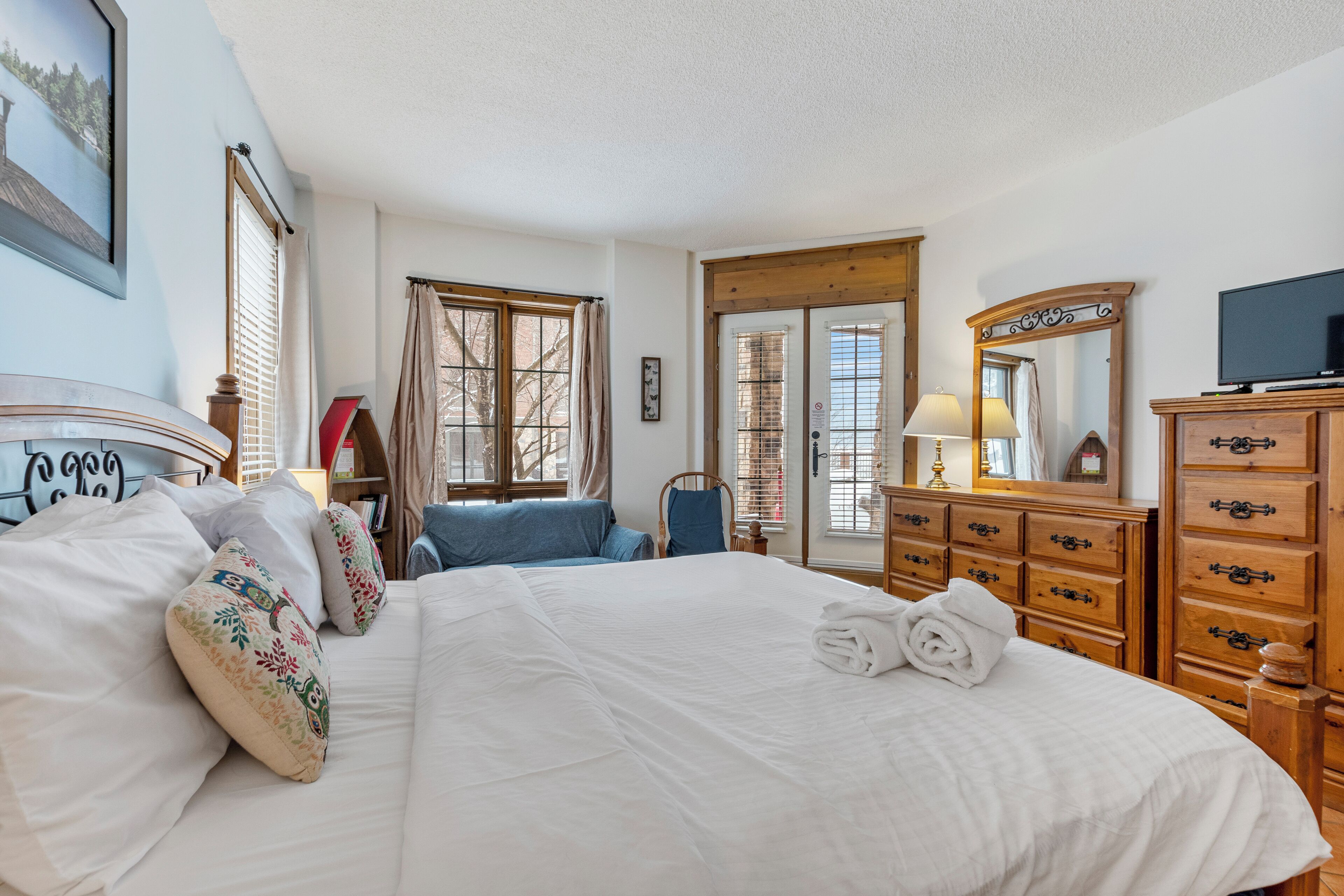 A well-lit hotel room with a large bed, wooden dresser, and a television.