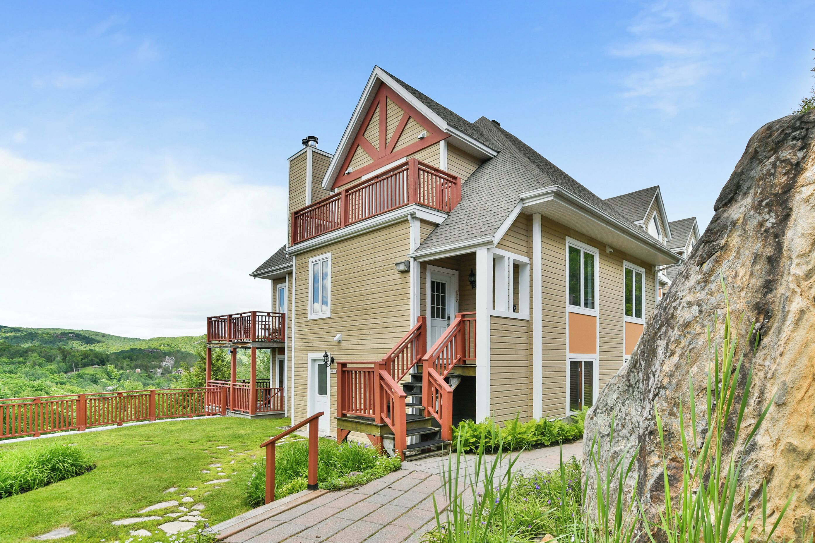 A two-story house with a balcony, a stone pathway, and a view of the surrounding landscape.