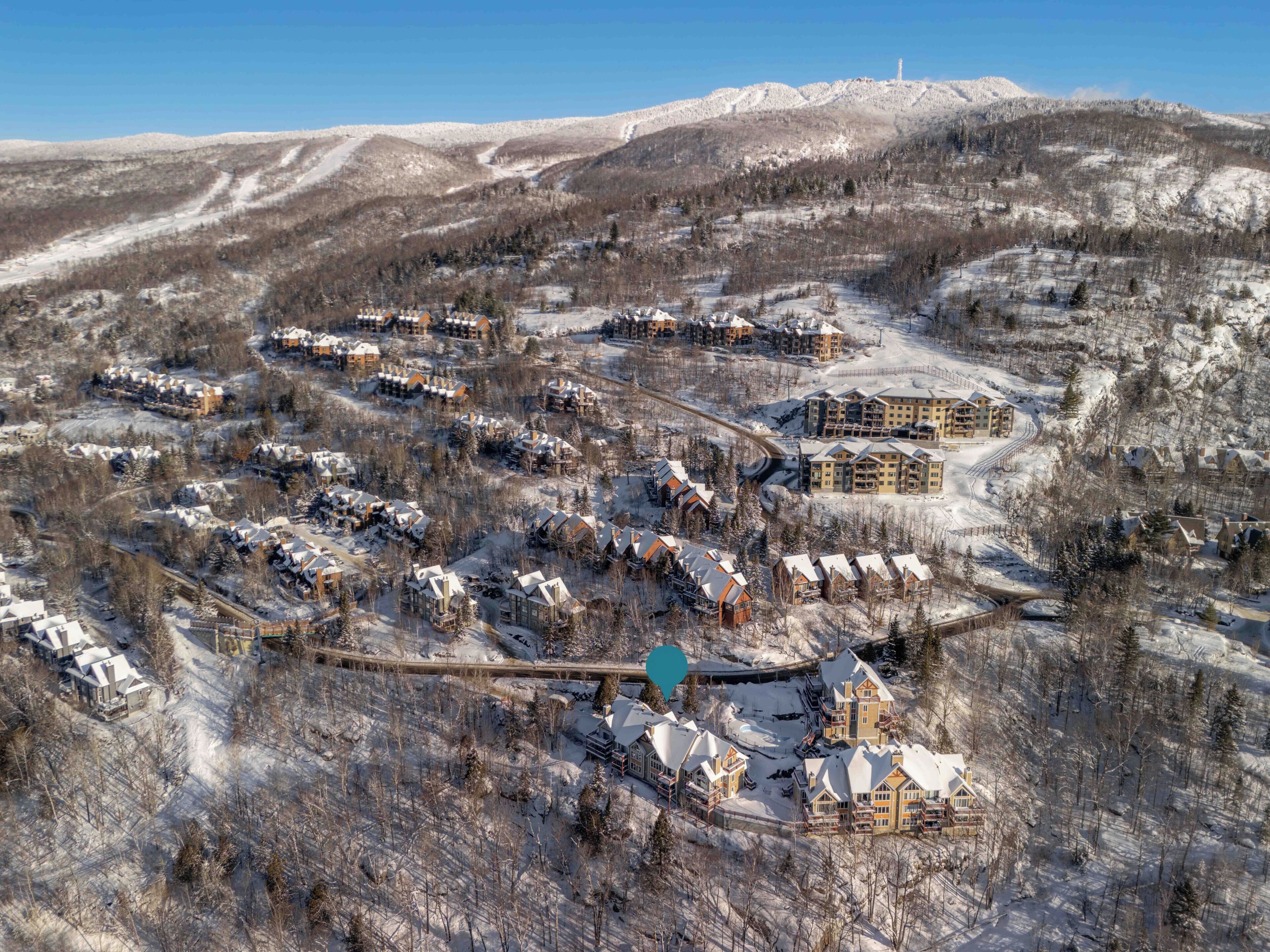 A snow-covered resort with multiple buildings, including a large lodge and smaller cabins, surrounded by mountains.