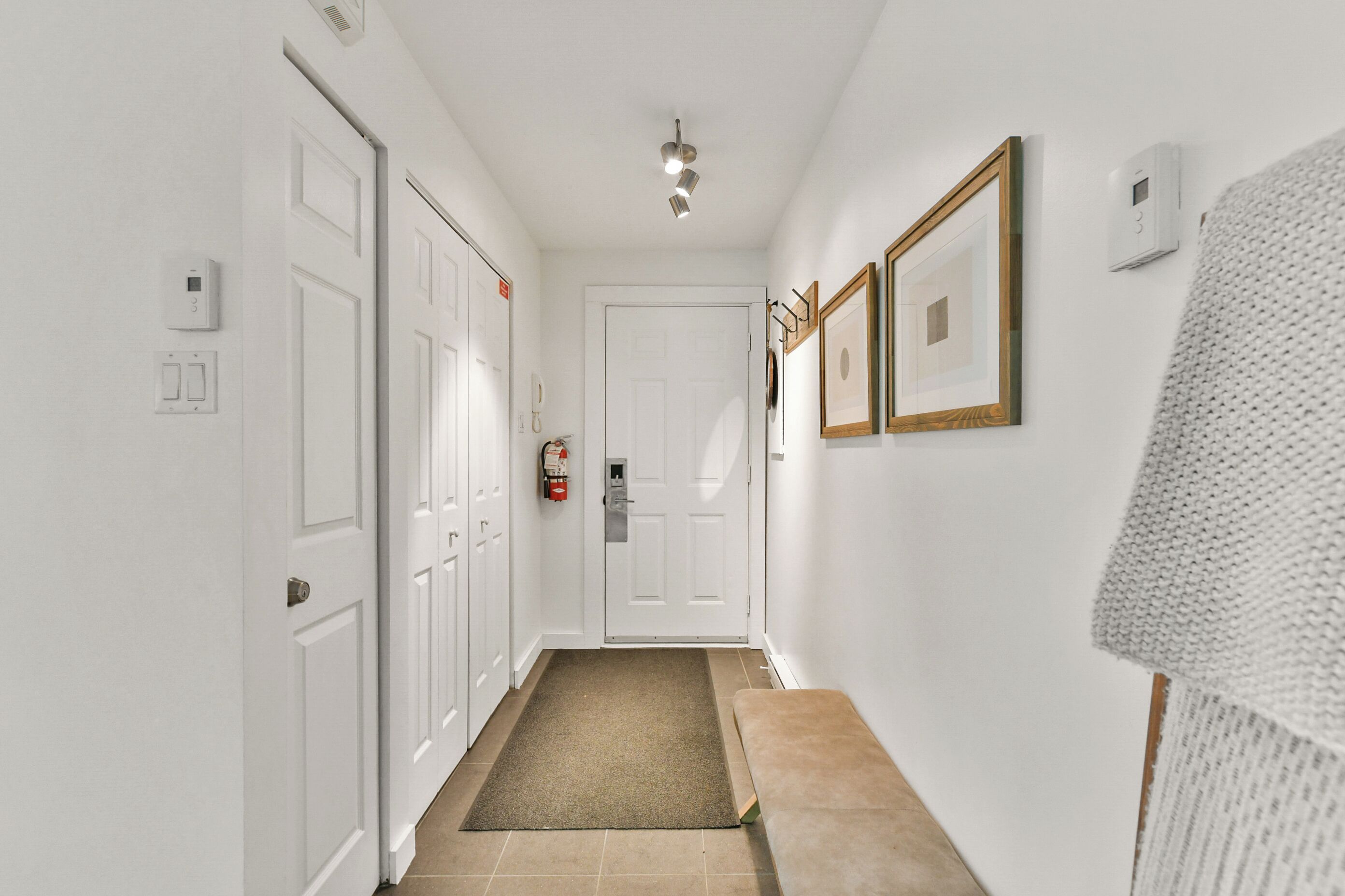 A hallway with white walls, a wooden bench, a door, and a fire extinguisher.