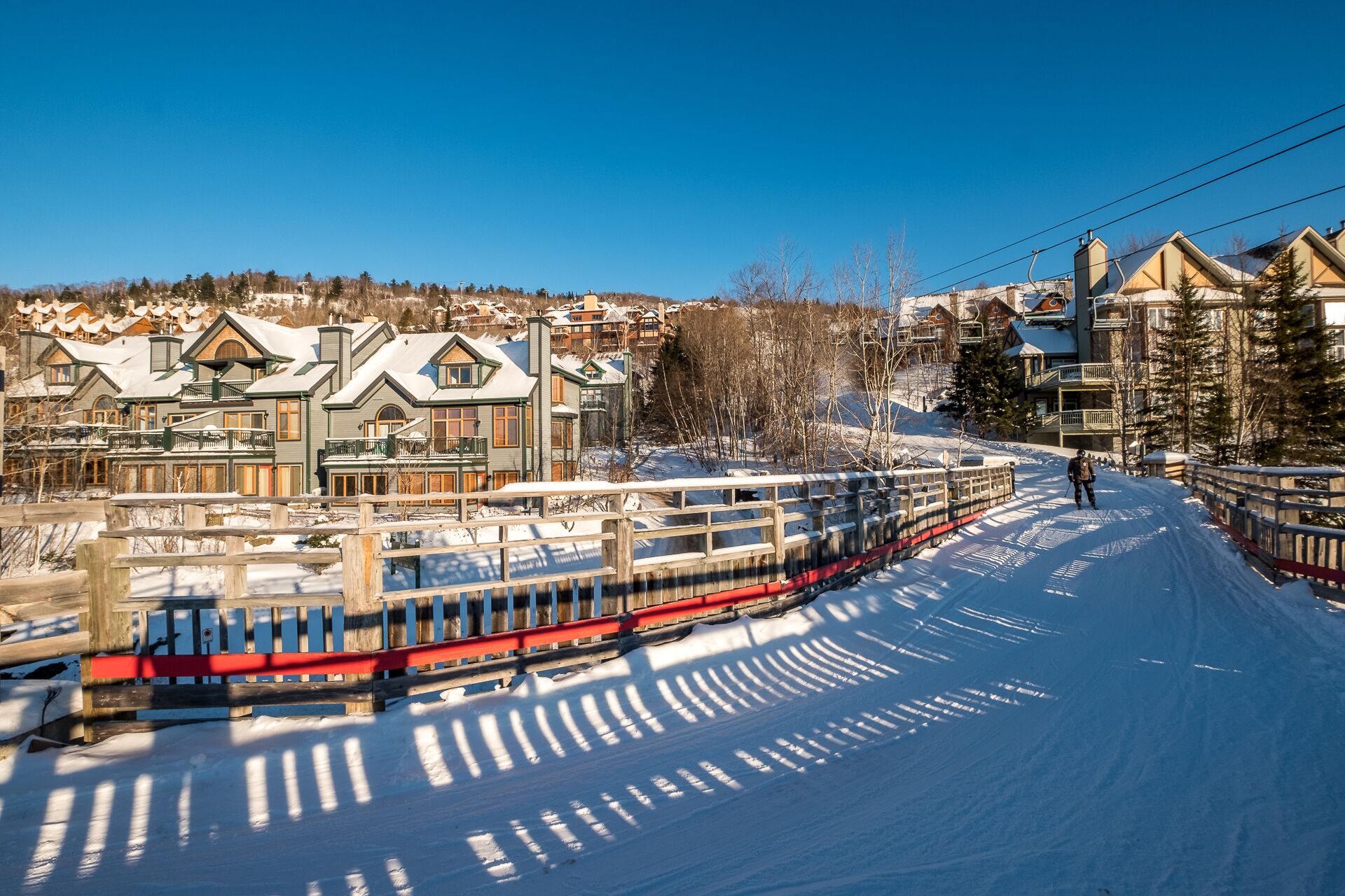 Un centro de esquí cubierto de nieve con un tren rojo y blanco, edificios de madera y un cielo azul despejado.