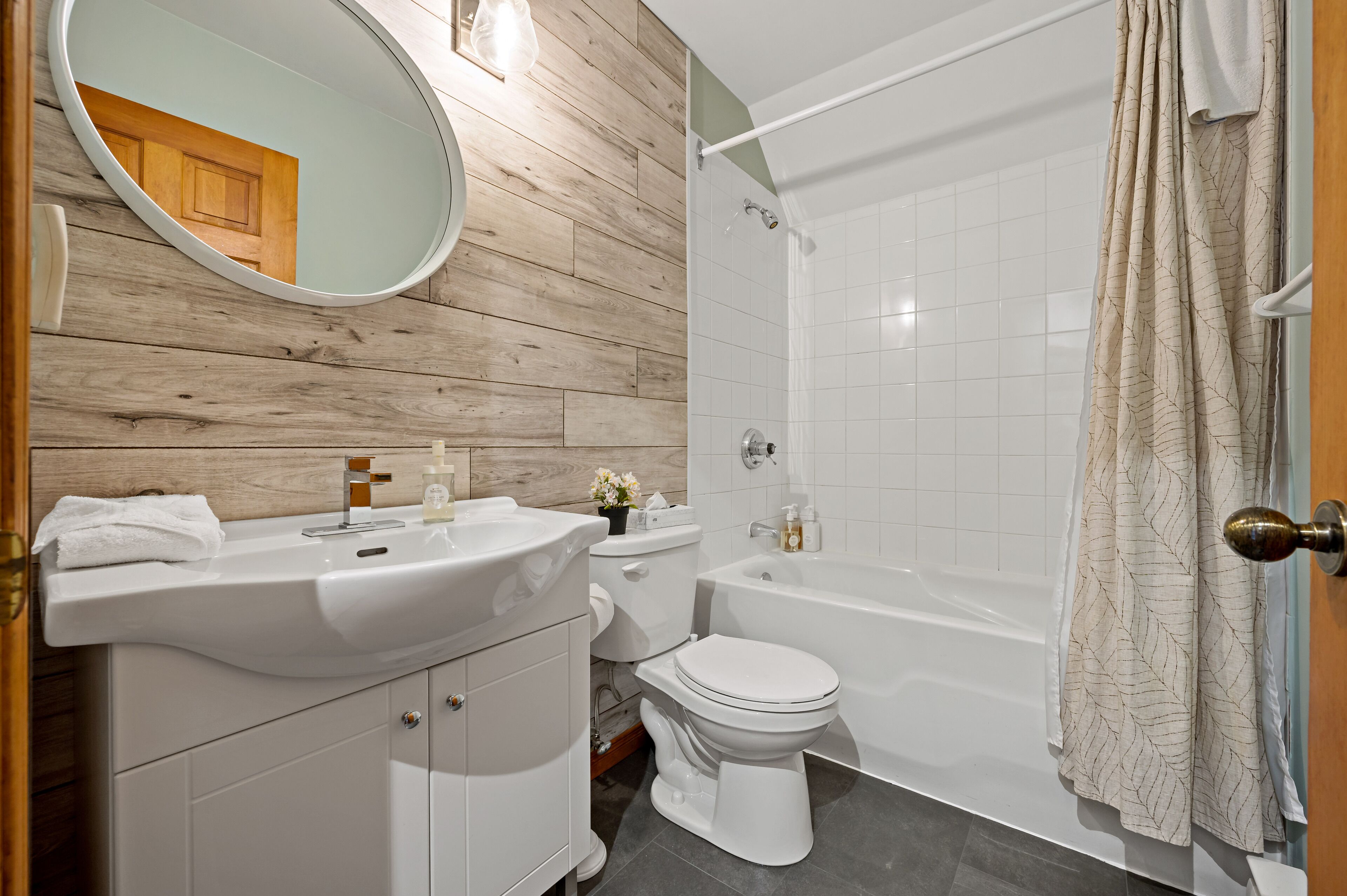 A bathroom with a wooden wall, a sink, toilet, and a bathtub.