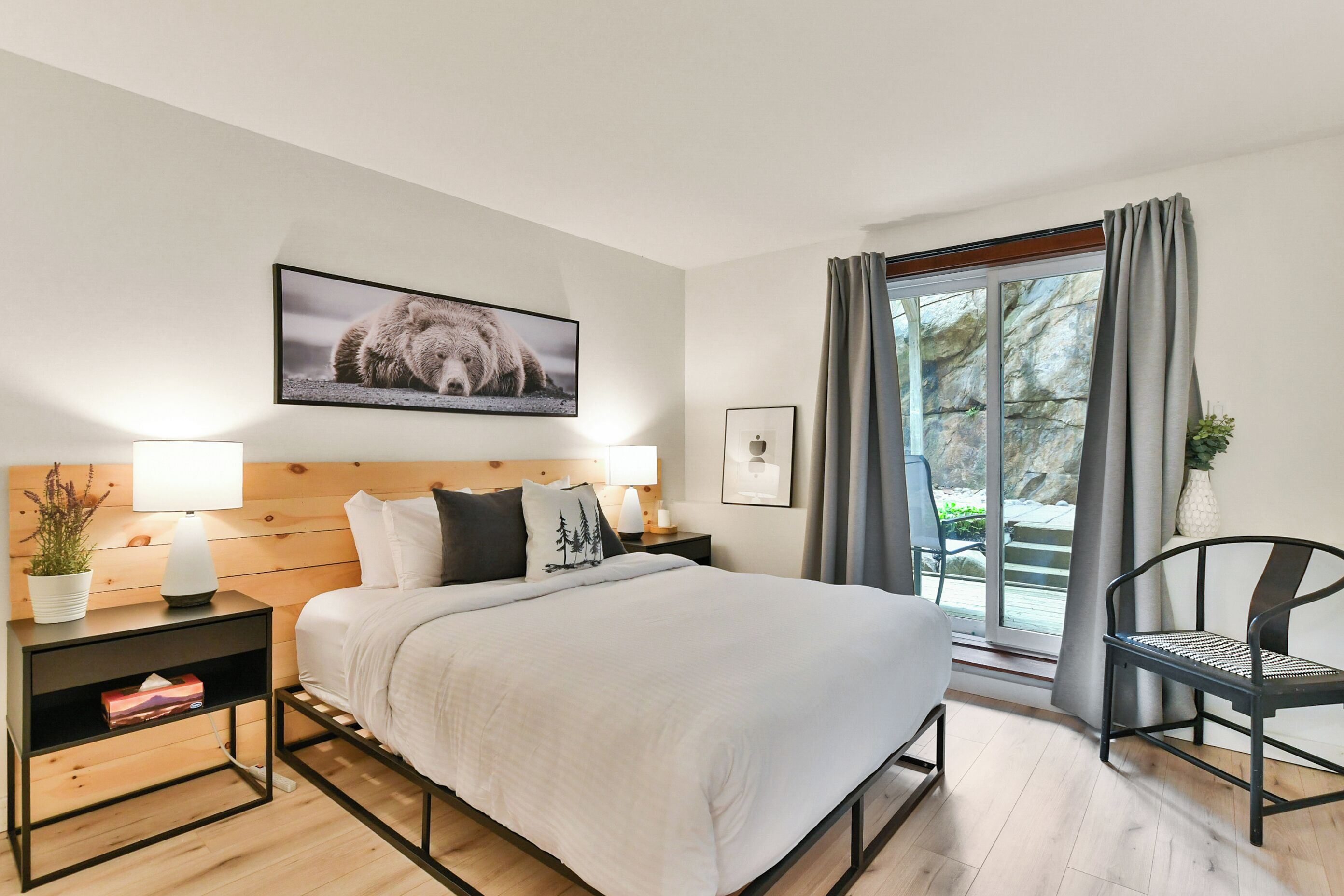 Una camera da letto con un letto, comodini, una sedia, una finestra con tende e un quadro appeso al muro.