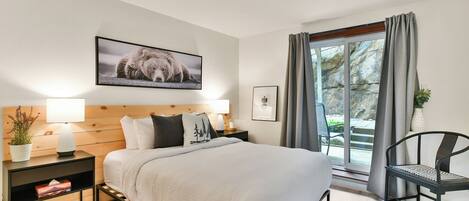 Una camera da letto con un letto, comodini, una sedia, una finestra con tende e un quadro appeso al muro.