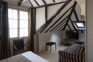 Una habitación con cama, una silla, una mesita, un televisor y una ventana con cortinas.