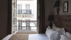 A hotel room with a bed, a view of a balcony with a railing, and a wall-mounted lamp. - Hôtel Saint-Louis Marais (Paris)