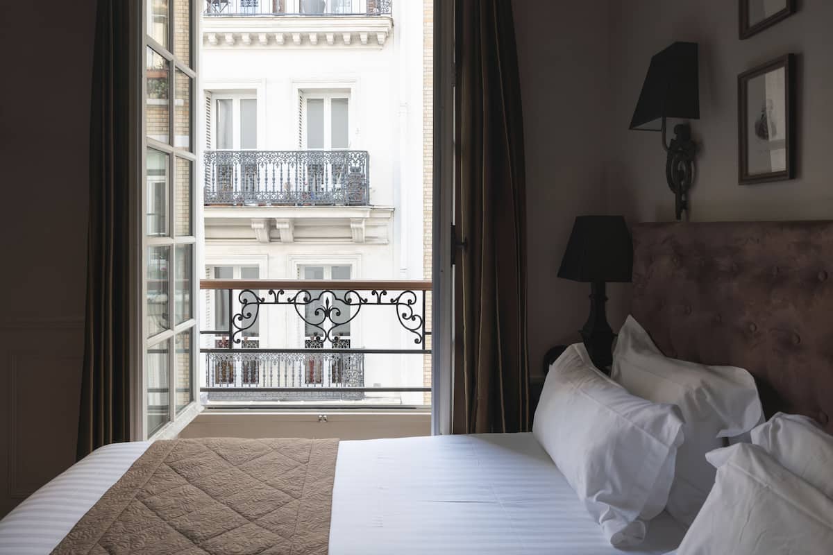 A hotel room with a bed, a view of a balcony with a railing, and a wall-mounted lamp.