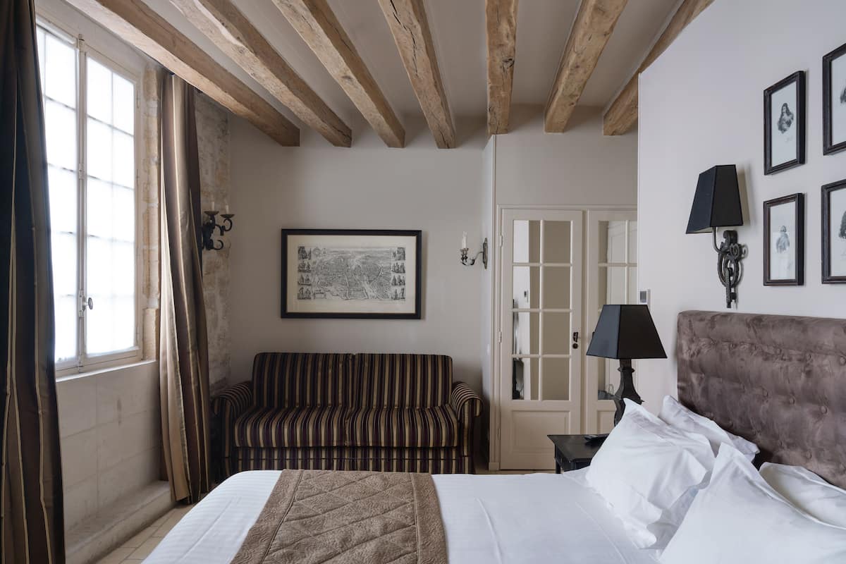 A hotel room with a bed, a striped sofa, a framed map on the wall, and a door with a window.